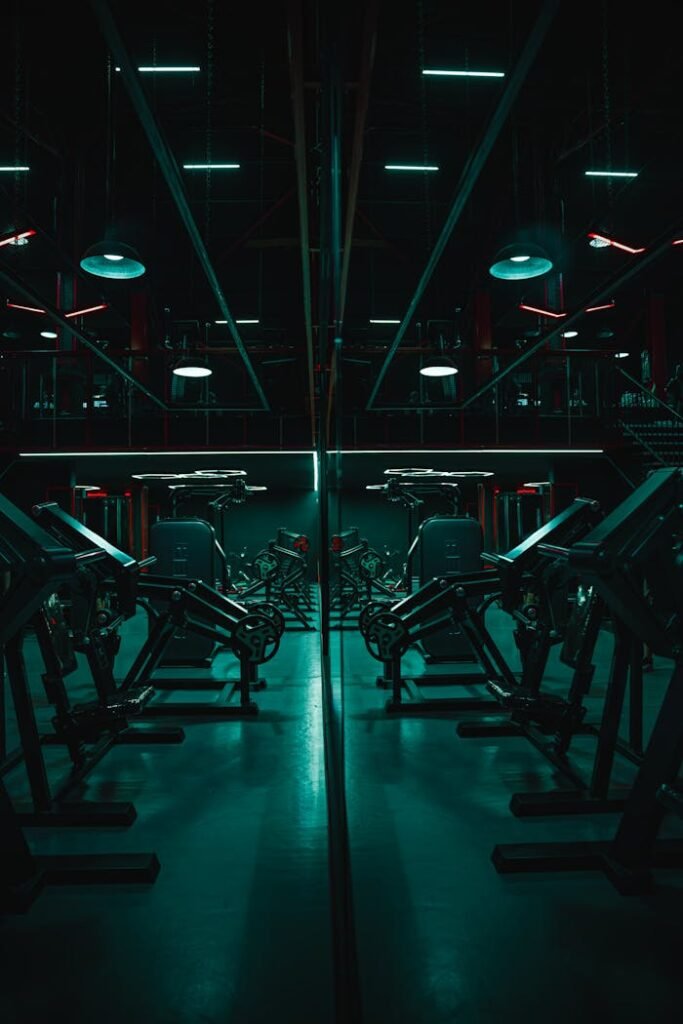 Dark, atmospheric gym with mirrored weightlifting machines and neon lighting.
